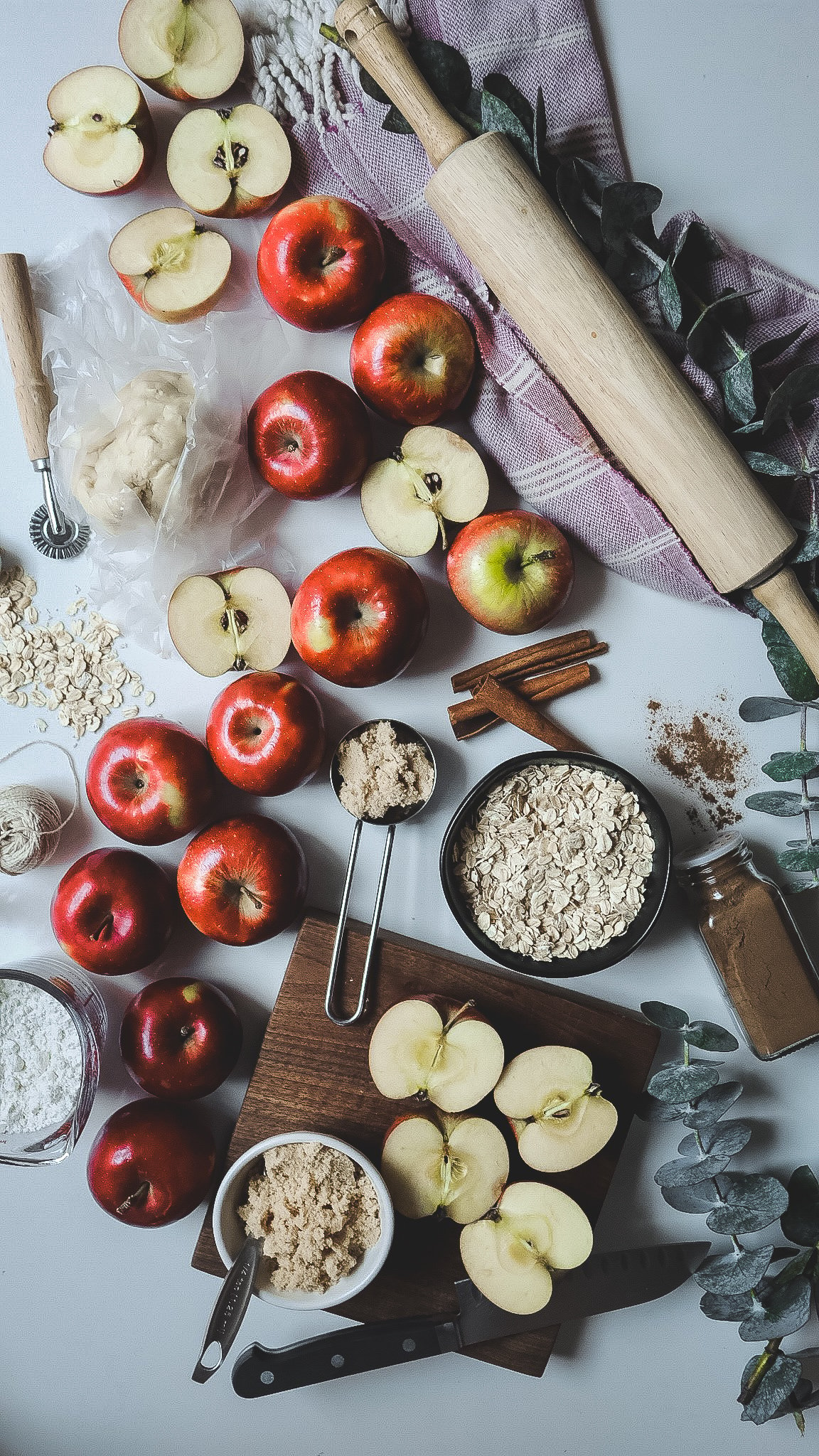 red apples, baking ingredients , a rolling bin and oats all styled on a counter top