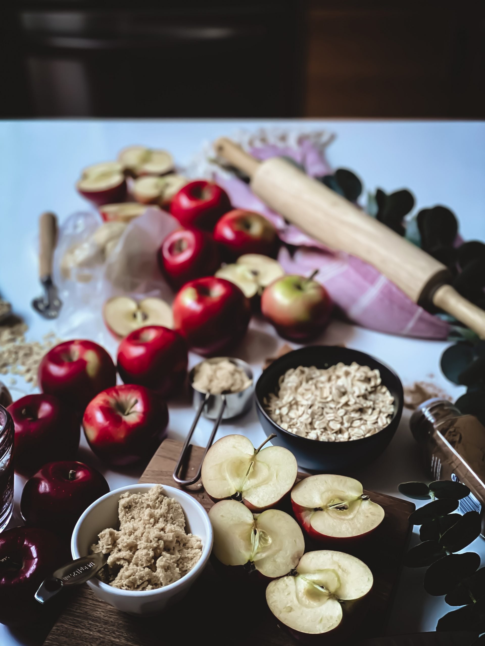 red apples, baking ingredients , a rolling bin and oats all styled on a counter top
