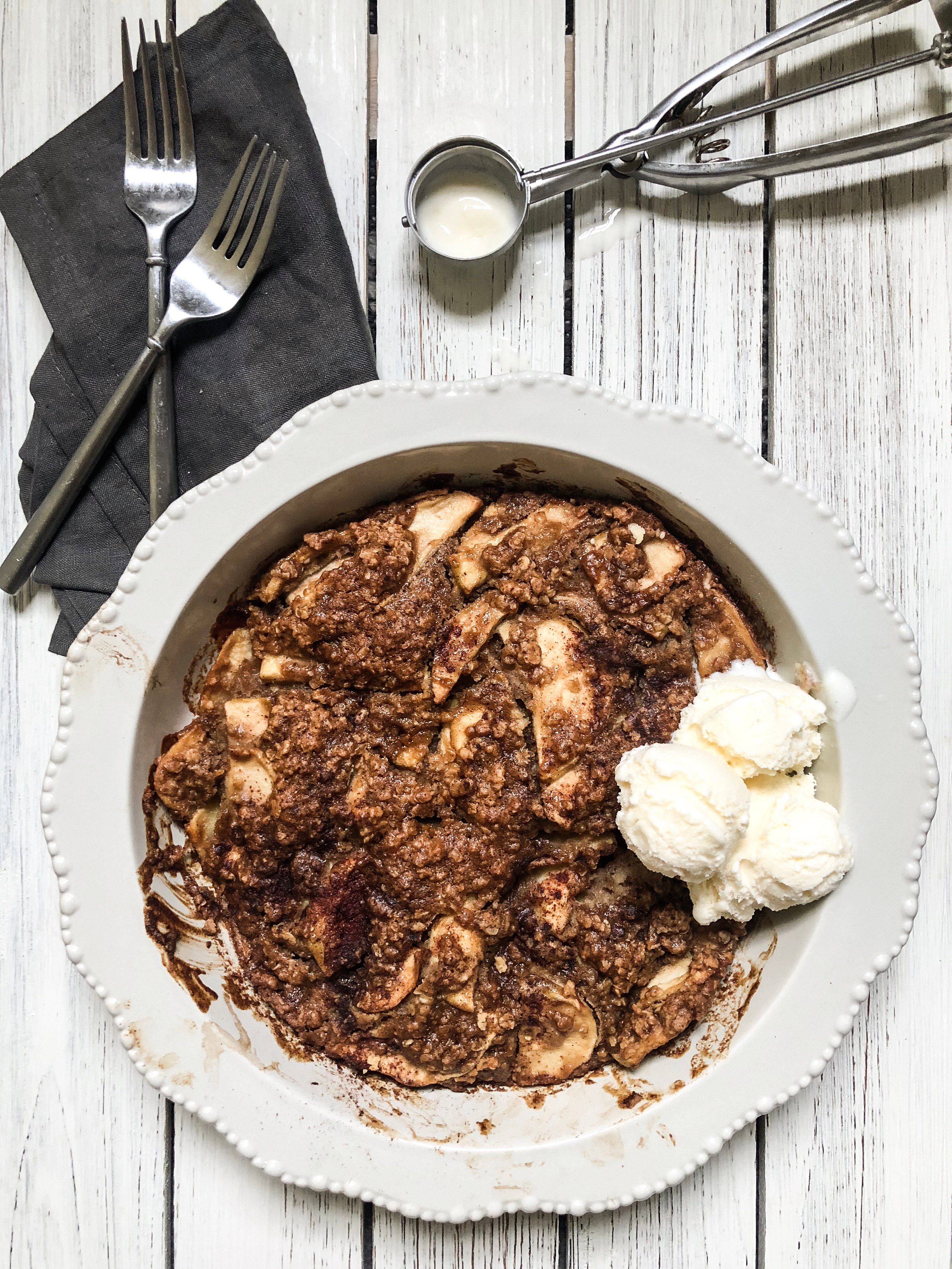 a pie plate filled with Apple Crisp with crunchy topping and ice cream, forks and spoons. 
