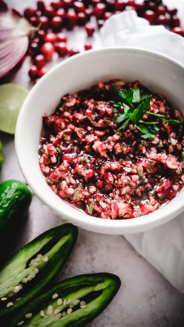 a white bowl with bright red cranberry salsa with jalapeños