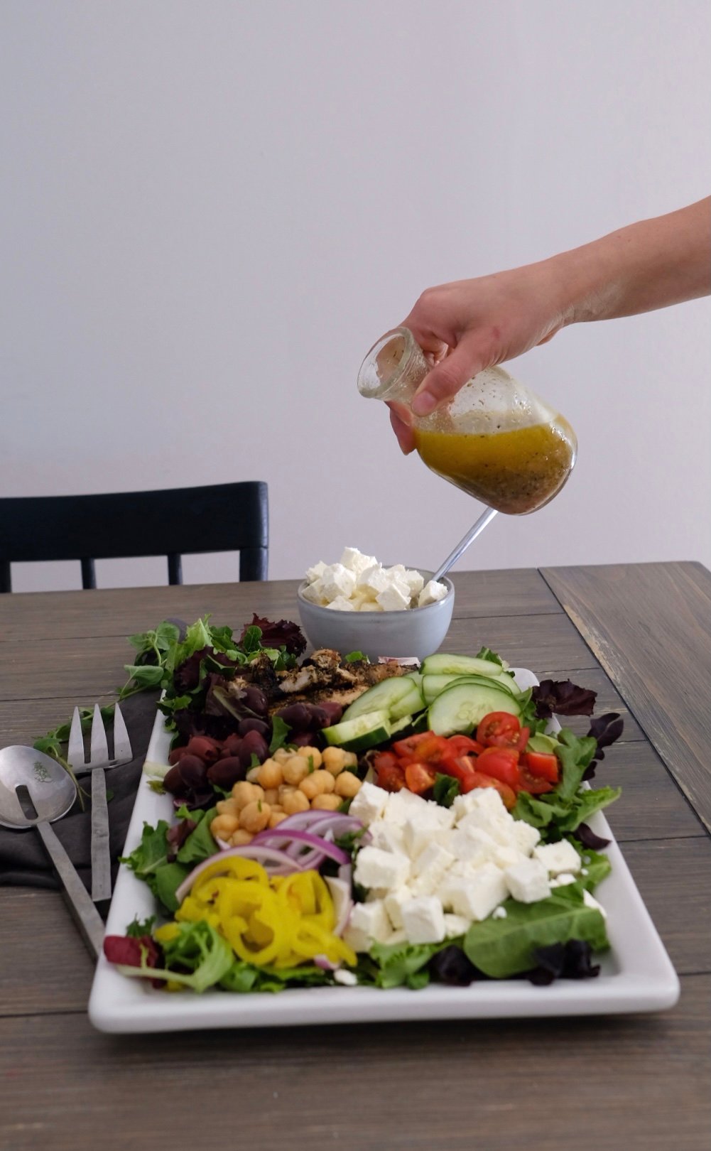 a hand holding a bottle of homemade greek oregano dressing over a greek salad. 