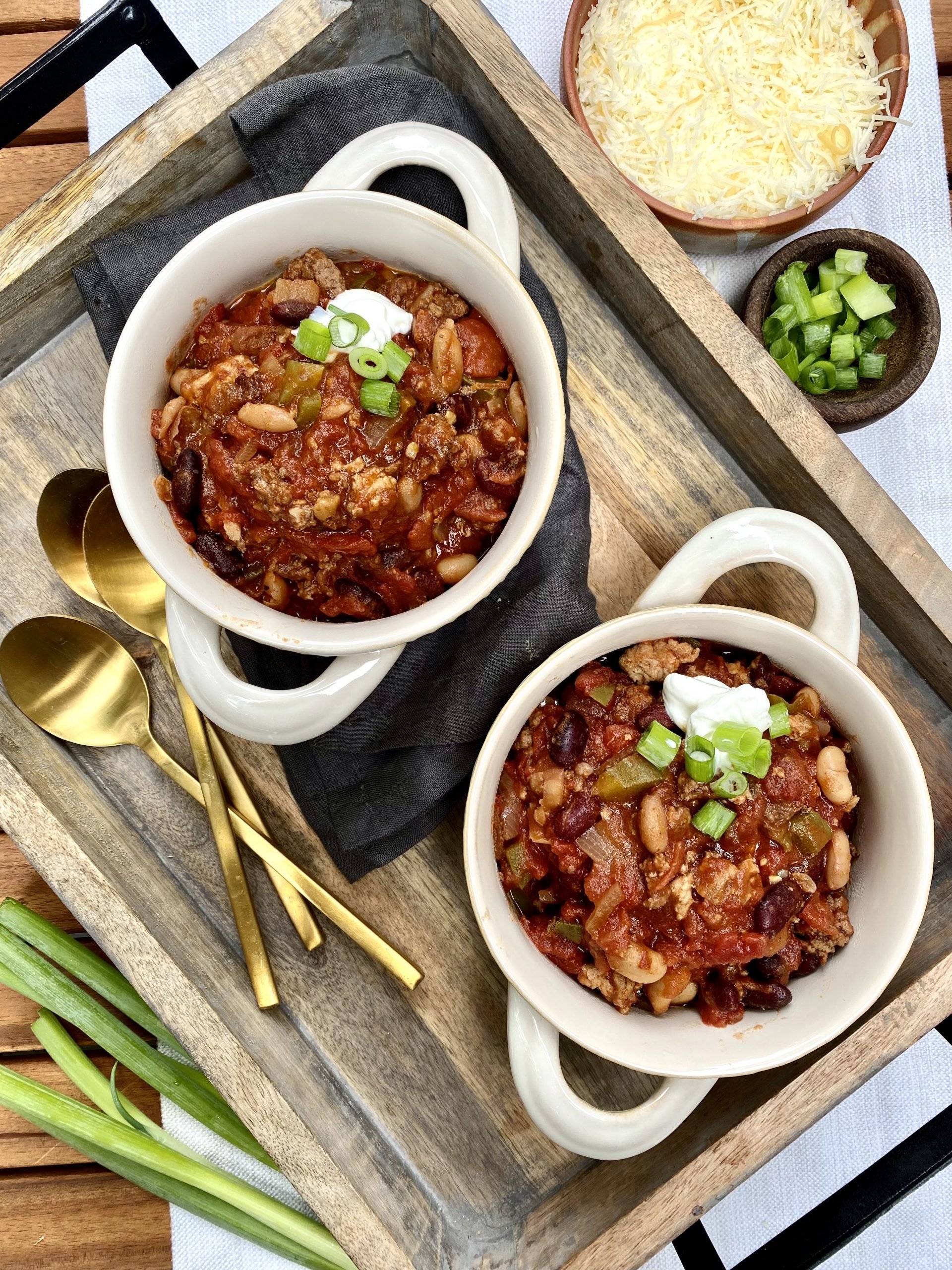 two bowls with chili with beans and ground beef garnished with cheese and green onions.