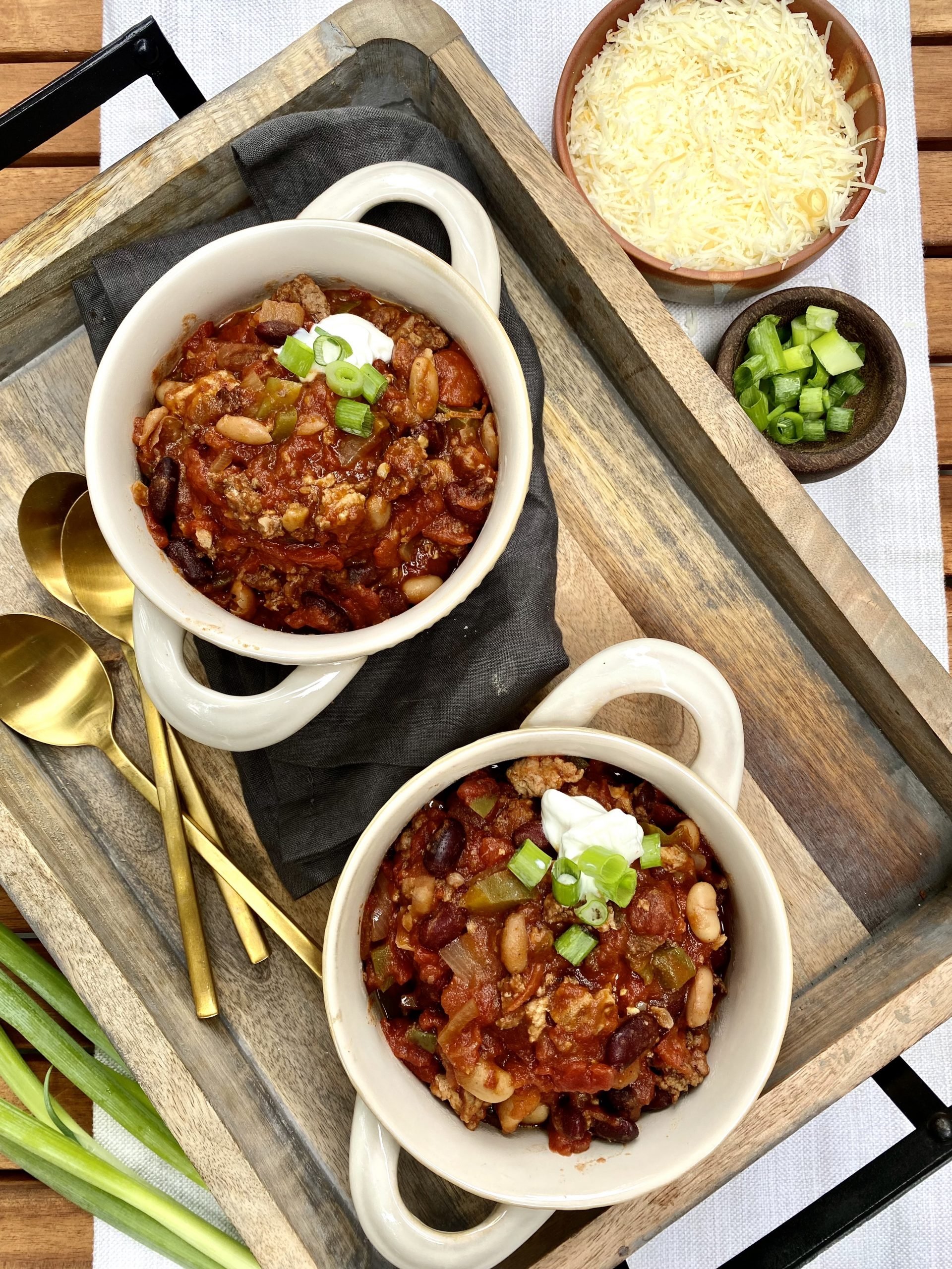 two bowls with chili with beans and ground beef garnished with cheese and green onions.