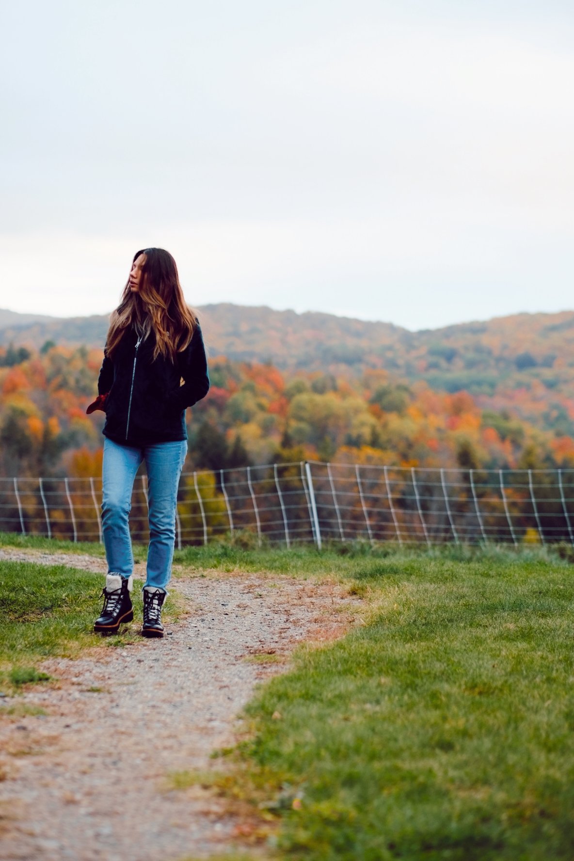 a woman walking in hiking boots, jeans and long brown hair hiking in the fall