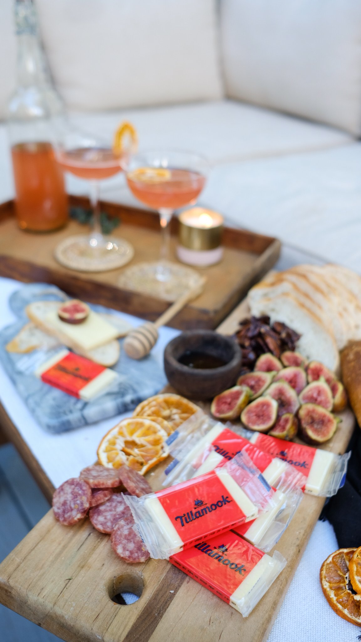 a cheese tray spread with cheeses, figs, nuts and brightly colored drinks