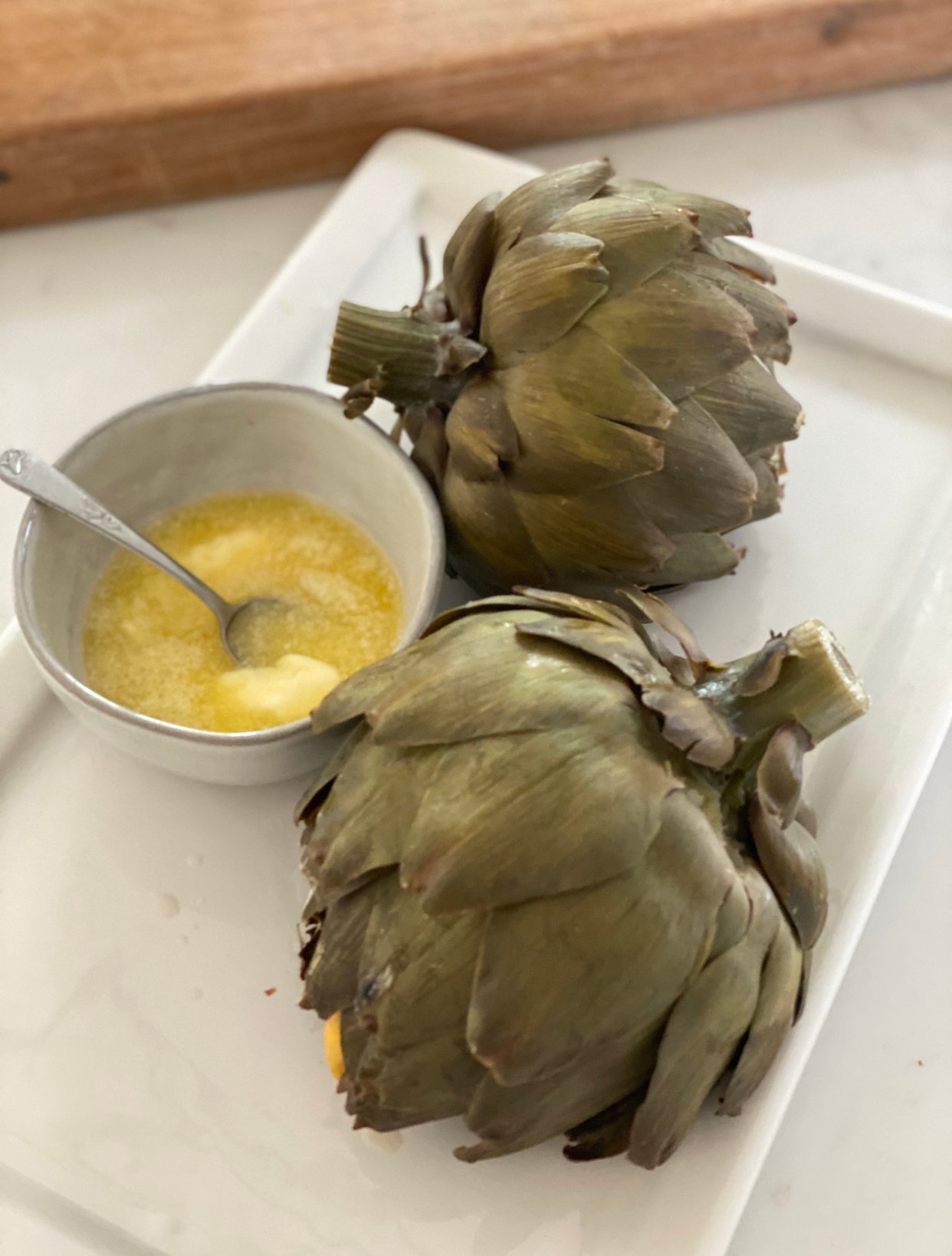 two steamed artichokes with butter on a tray. 