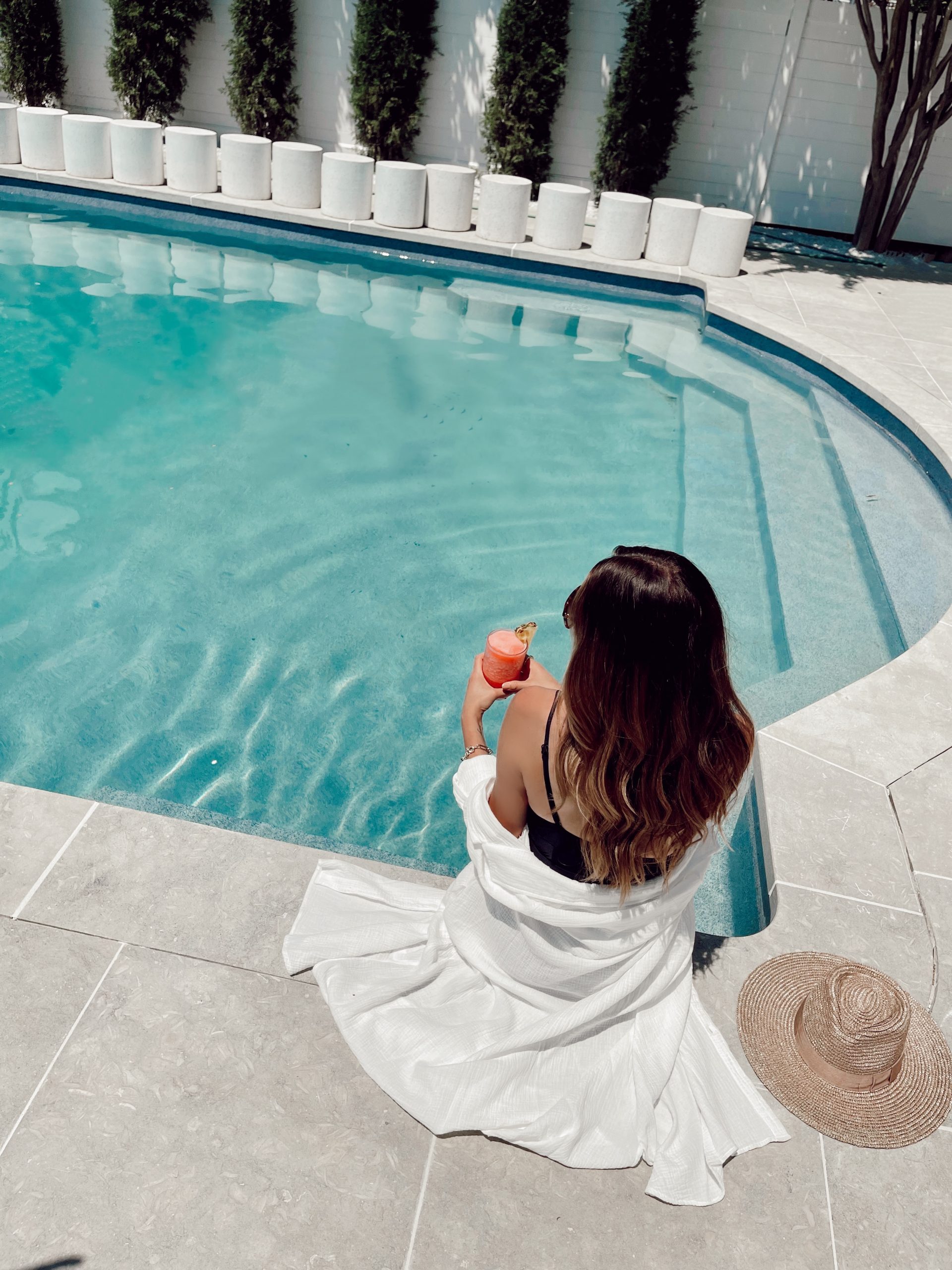 a woman sitting by the pool at the St. Laurent Hotel with long brown hair and a pink drink.