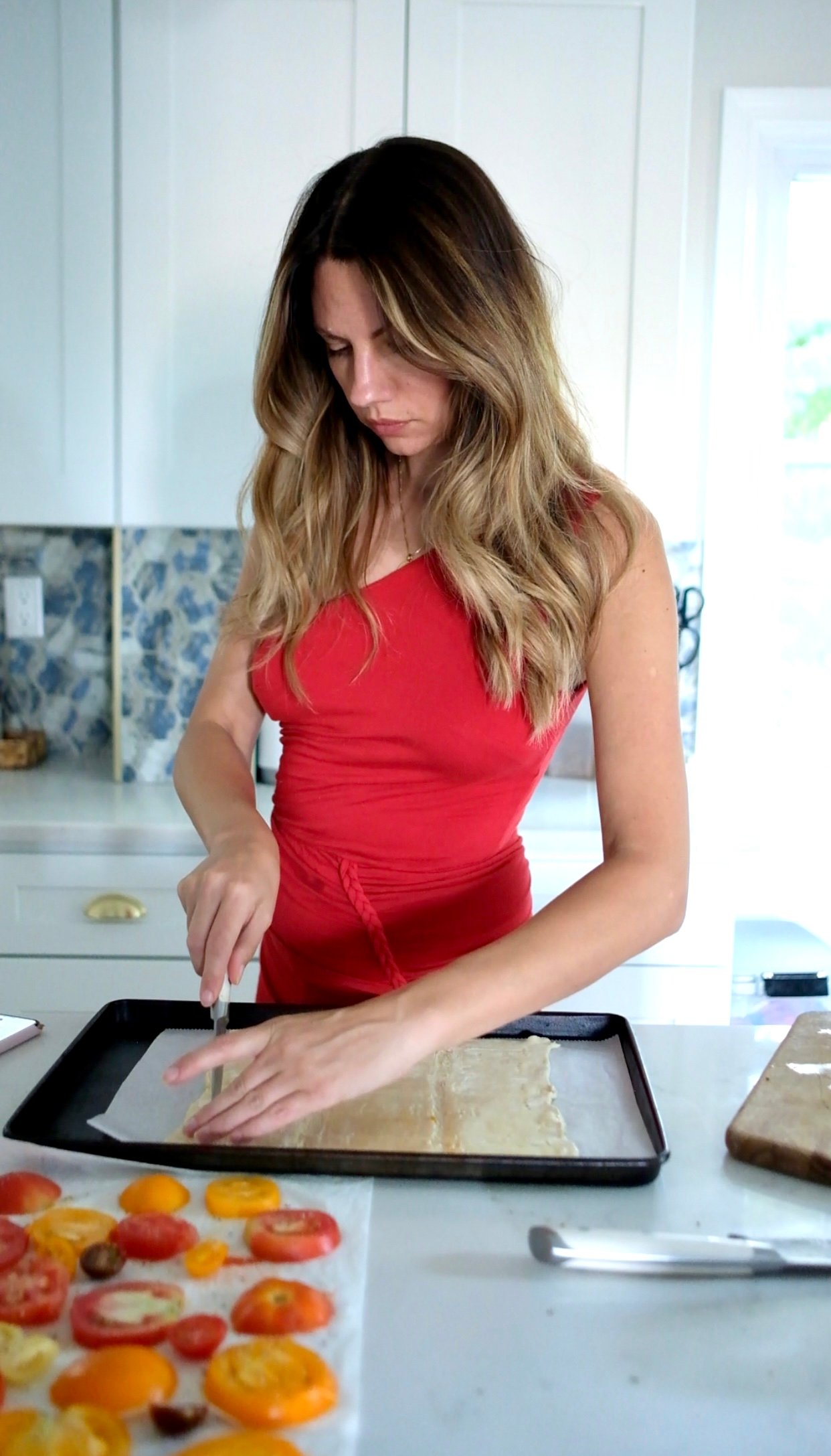 a woman cutting a puff pastry for a tomato tart recipe. 