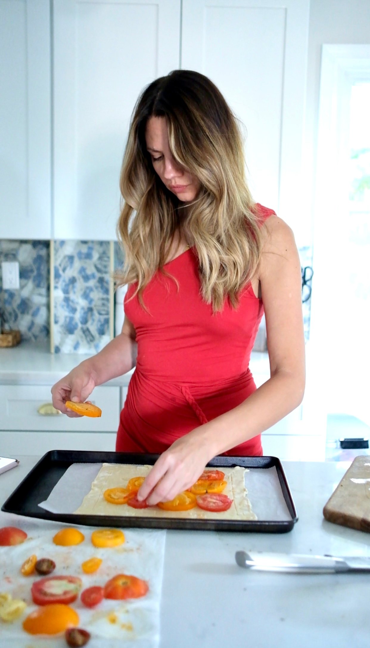a woman in a red dress makes a tomato tart recipe. 