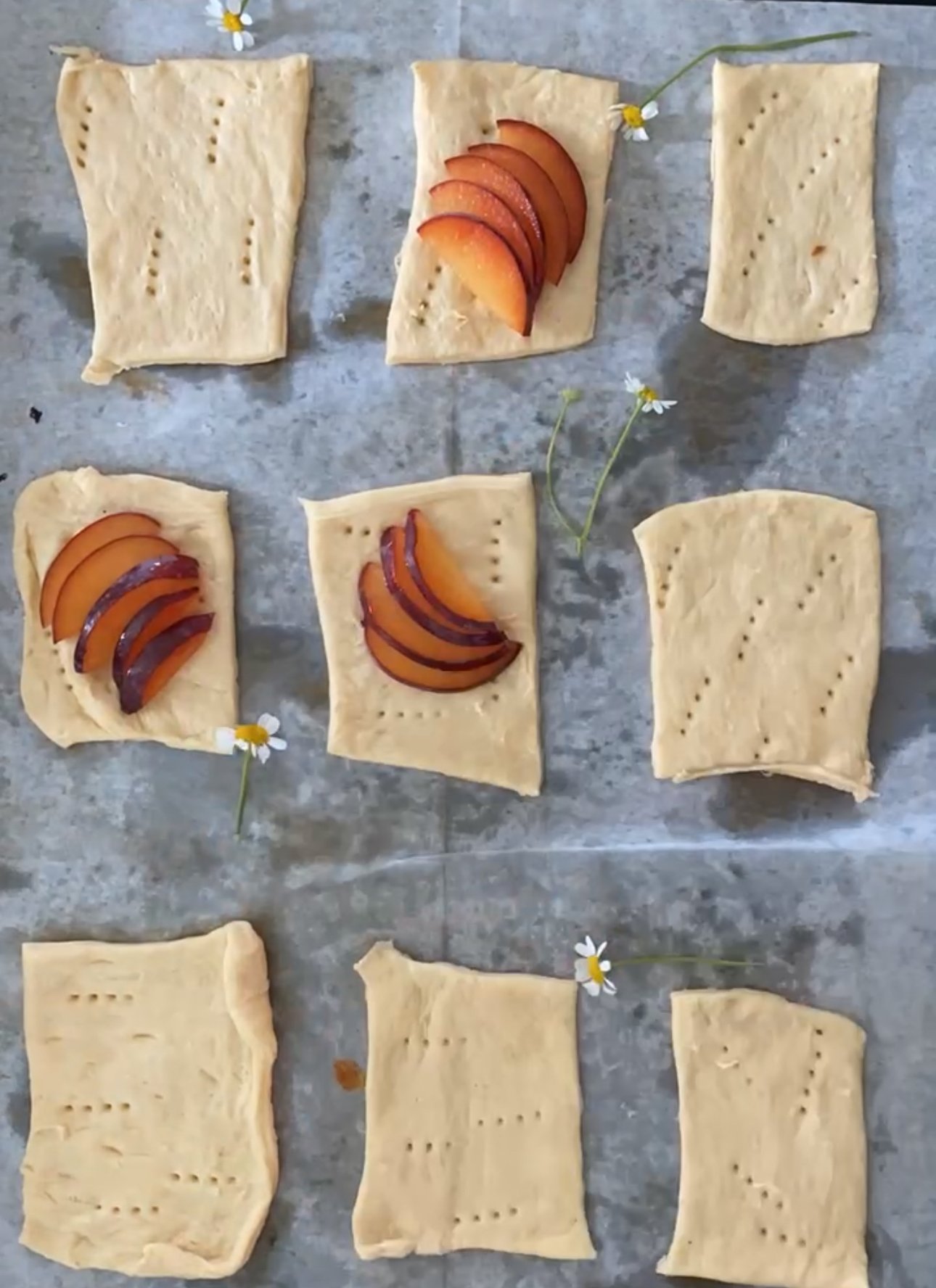 puff pastry tarts are rolled out on a baking sheet with plums starting to be assembled for plum tarts. 
